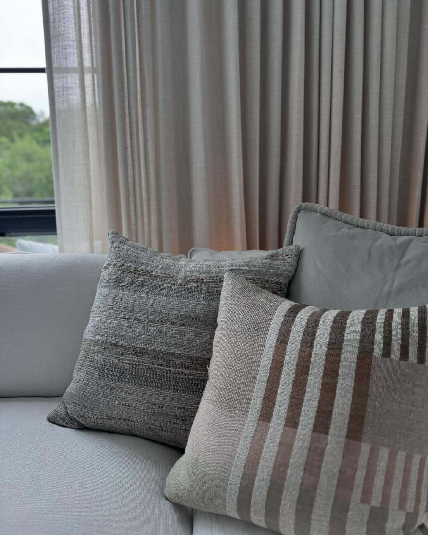 Natural linen sofa layered with pillows in ivory, taupe, and washed neutrals beneath soft daylight