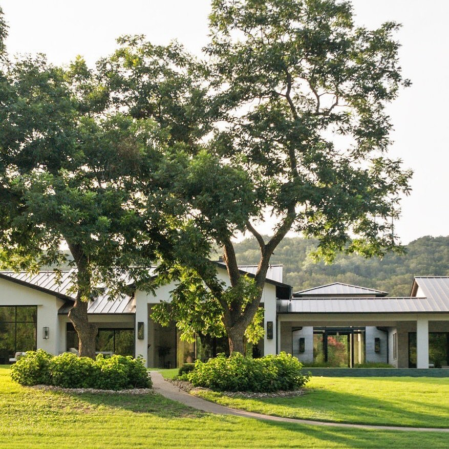 Front elevation of a limestone ranch house with gabled metal roofs in golden-hour light