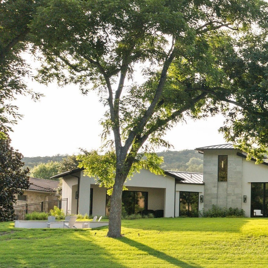 Limestone tower volume of a modern Hill Country ranch glowing at golden hour beneath live oaks