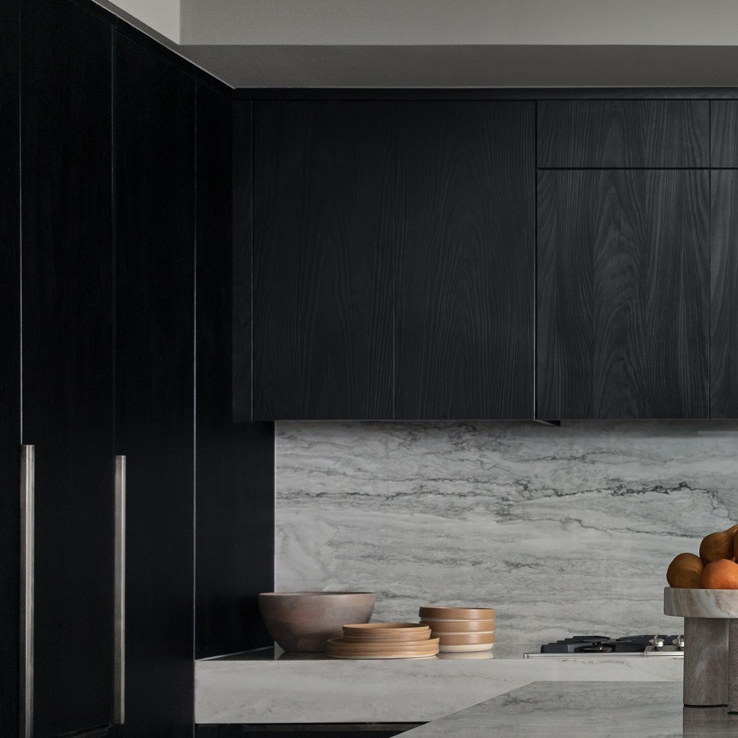 Corner of a dark charcoal kitchen styled with terracotta ceramics on honed stone counters