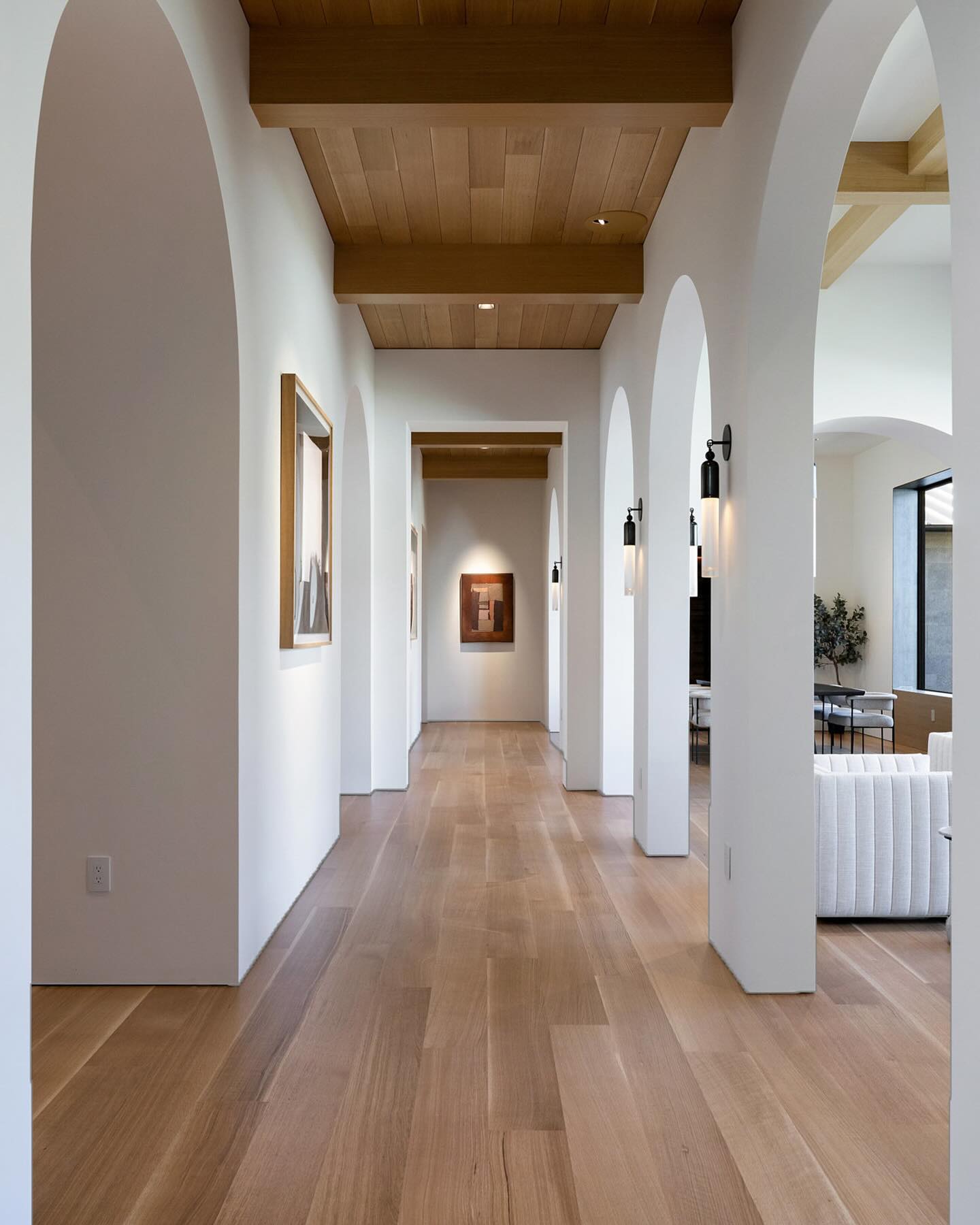 Bright gallery hallway of white plaster arches with oak beam ceiling