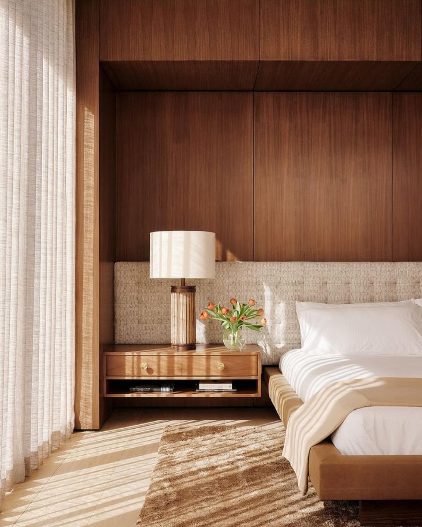 Sunlit bedroom with walnut paneling, woven boucle headboard, and sheer linen drapery