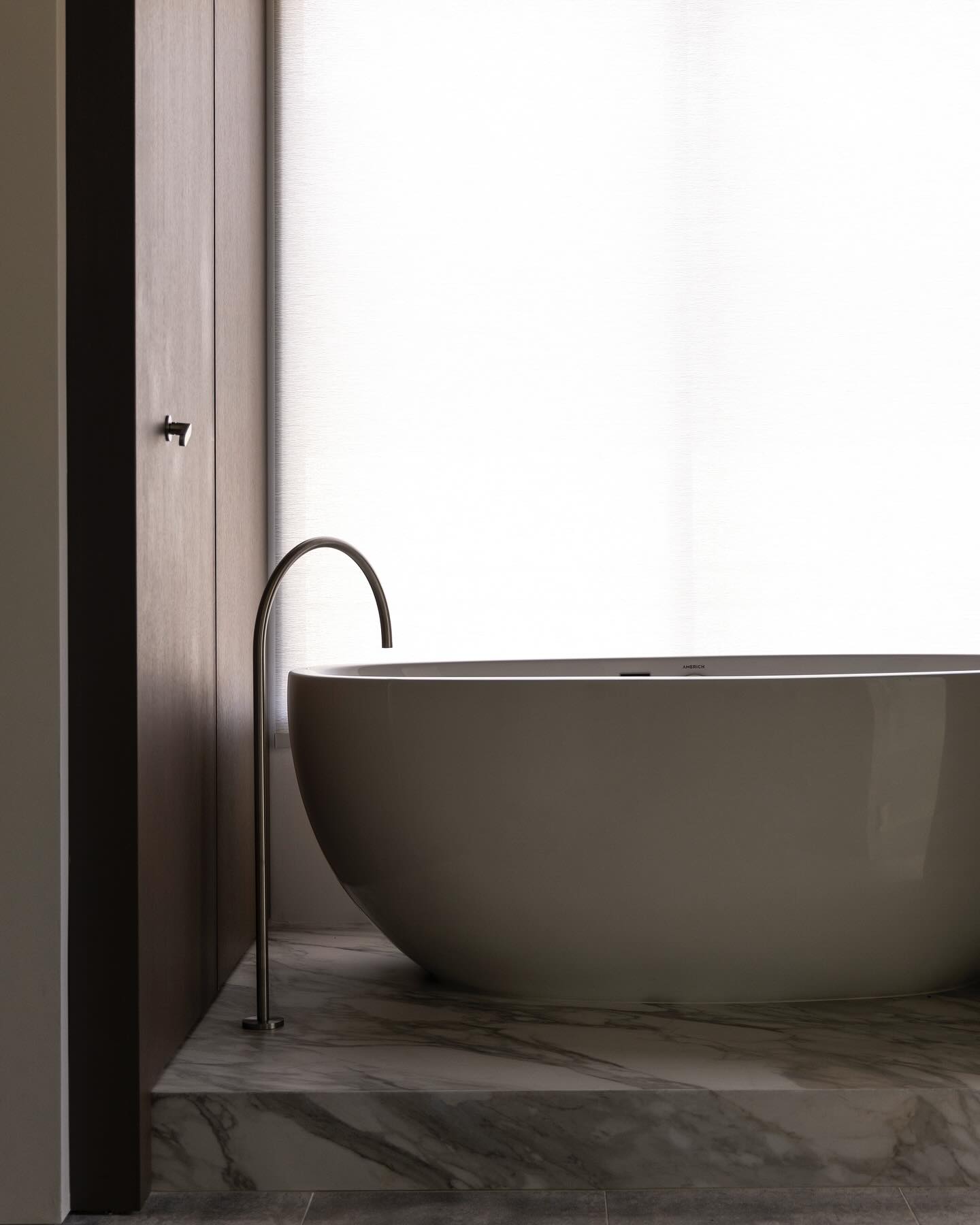 Sculptural white soaking tub on a marble plinth against dark oak paneling