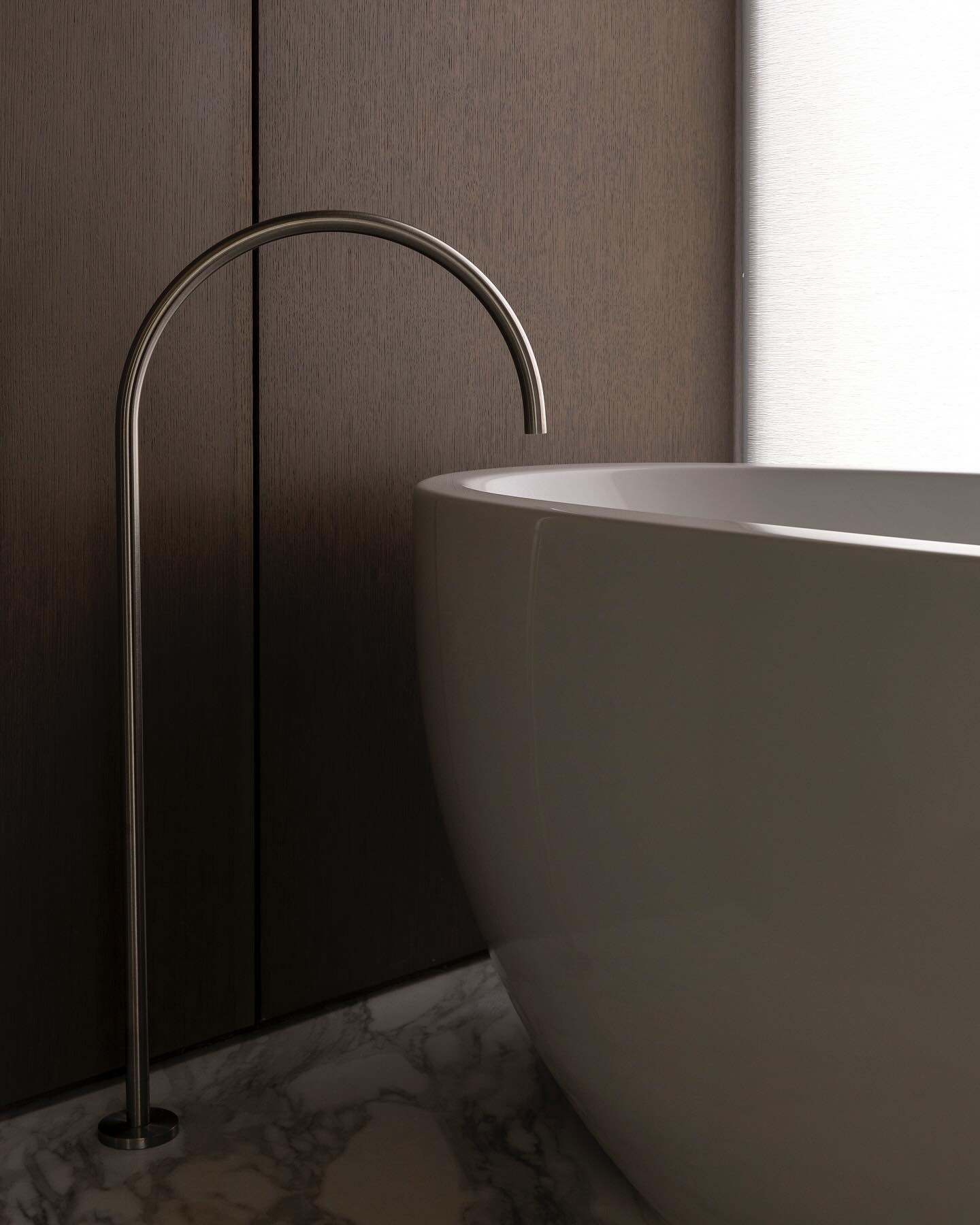 Arched polished-nickel tub filler curving over the rim of a sculptural white tub