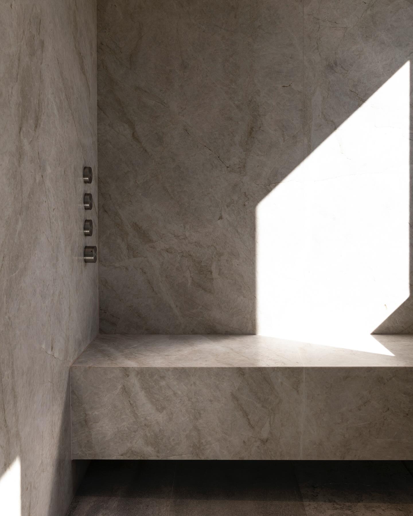 Quartzite wet-room shower crossed by a diagonal shaft of sunlight