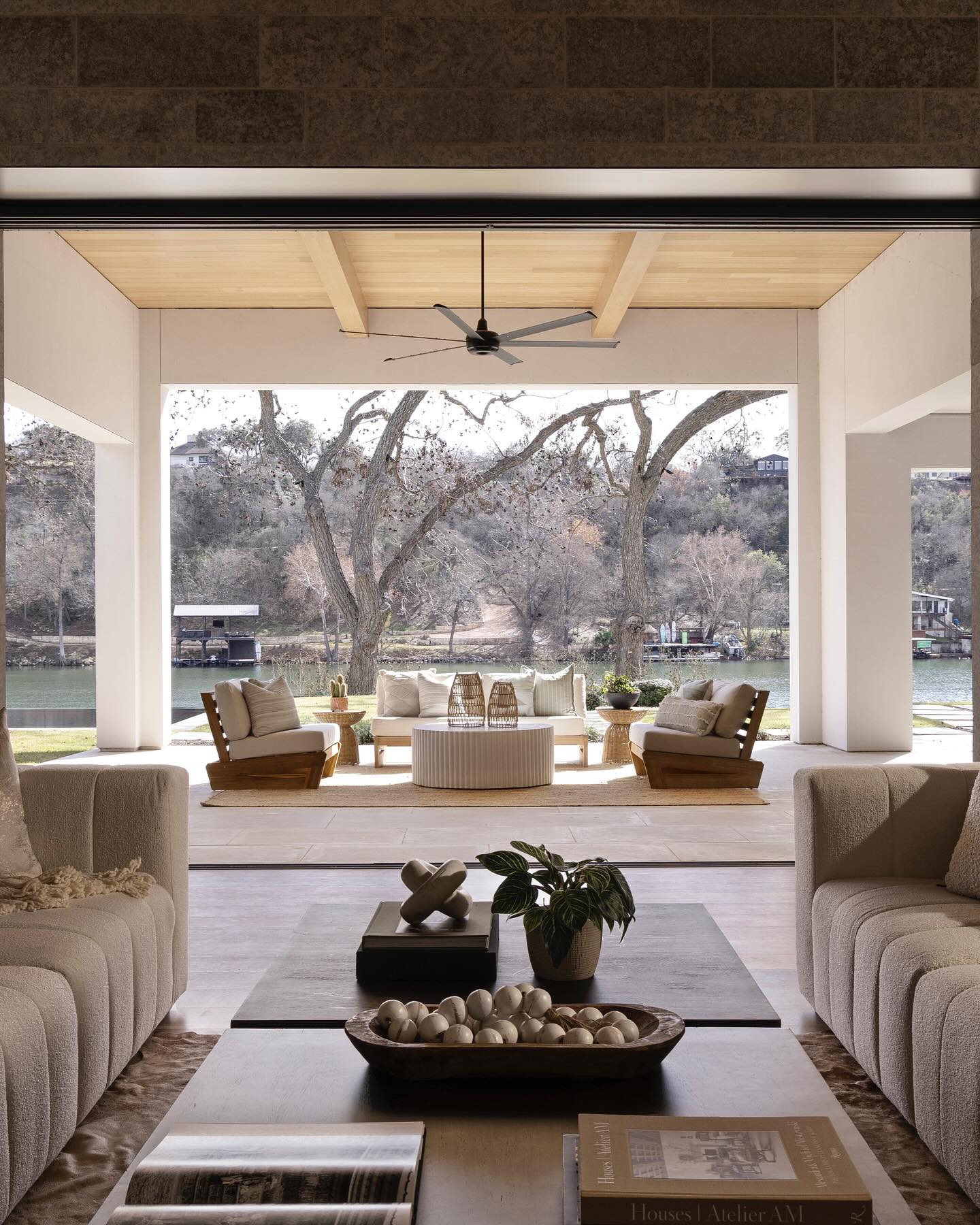 Lakeside living room with cream boucle sofas opening through retracted glass walls to a covered terrace over Lake Austin