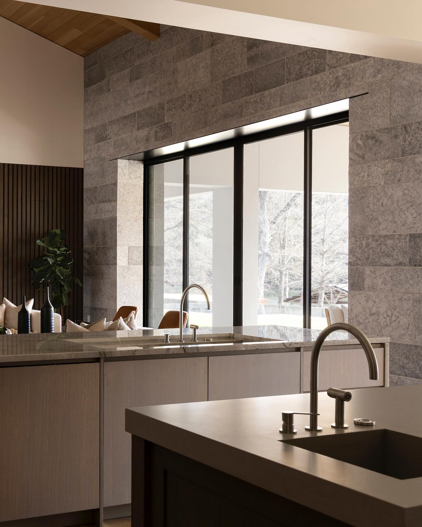 Kitchen with honed stone counters set against a limestone block wall and black steel doors opening to the landscape