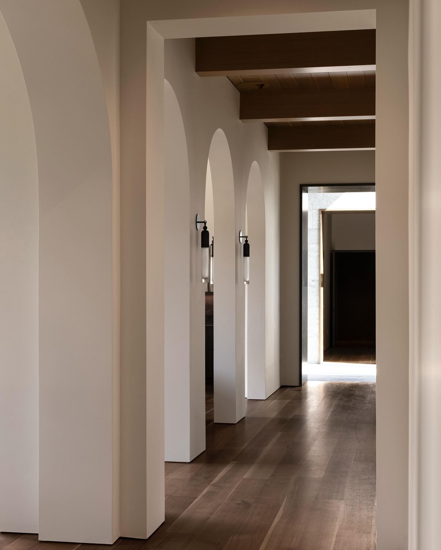 Sunlit hallway of white plaster arches with bronze sconces casting soft afternoon light