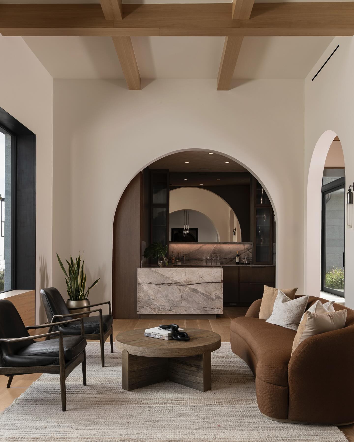Lounge with curved rust boucle sofa and plaster arch opening to a stone bar