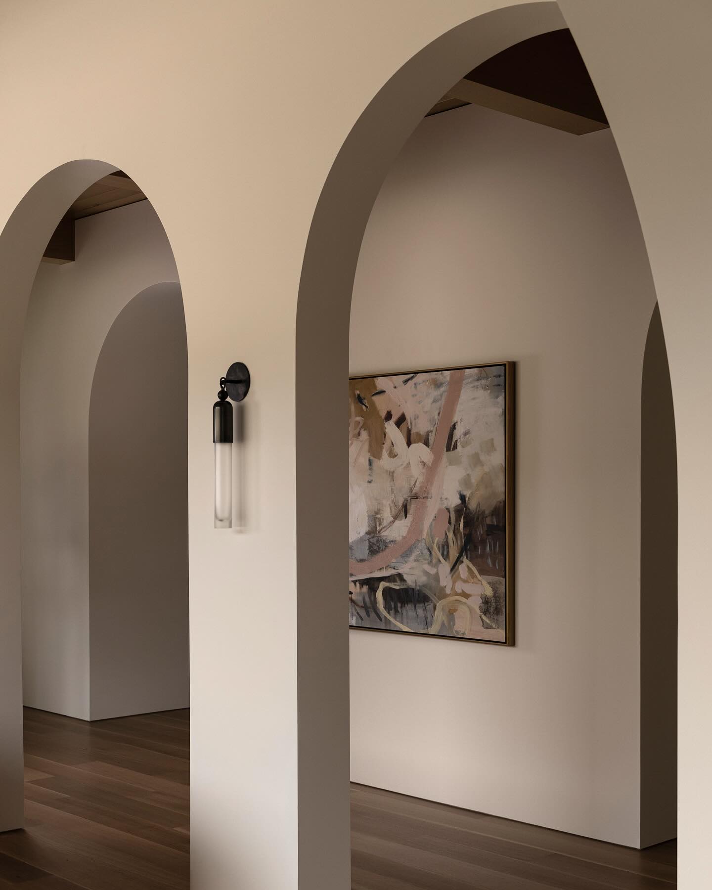 White plaster arch framing an abstract painting in a brass frame, hung on a softly lit wall